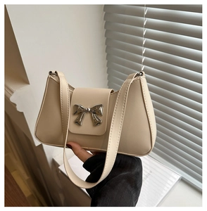 Detail of cream shoulder bag featuring a silver metal bow and smooth premium texture