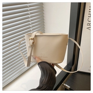 Close-up of litchi texture on cream bucket bag with gold hardware and logo detail