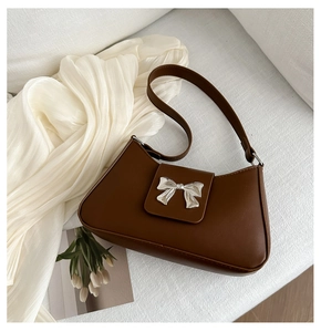 Close-up of brown PU leather shoulder bag featuring a decorative silver metal bow clasp