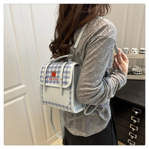 Detail of blue plaid mini backpack with red apple embroidery on a person's back
