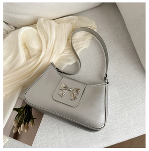 Detail shot of a silver metallic shoulder bag with a stylish metal bow on silk background
