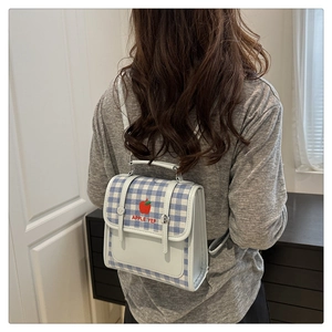Close-up of a blue and white gingham backpack with red apple embroidery on a female model