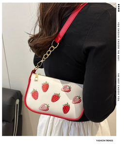 Detail of white strawberry print shoulder bag with red trim and gold chain strap