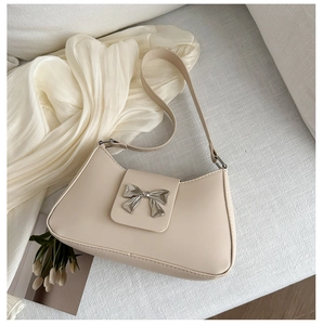 Close-up of beige half-moon bag with silver metal bow detail and smooth leather texture