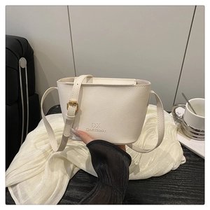 Close-up of a white lychee leather mini bucket bag with gold buckle on a wooden desk