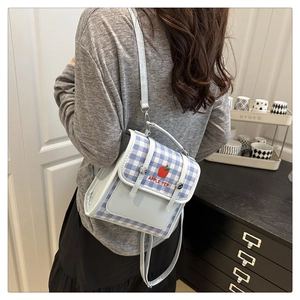 Detail of blue and white plaid backpack featuring red apple embroidery and adjustable strap