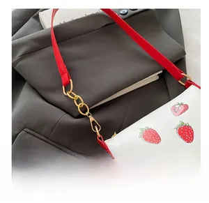 Close-up of strawberry print shoulder bag with red strap and gold metal hardware