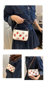 Detail of white strawberry print underarm bag featuring brown trim and gold chain strap