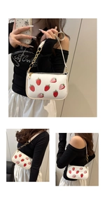 Detail of white strawberry print underarm bag with gold chain strap and metal zipper