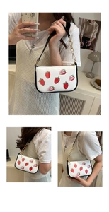 Detail of white shoulder bag featuring strawberry print and gold metal chain strap