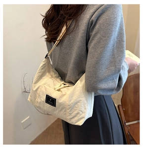 Detail of off-white wrinkled nylon crossbody bag with black brand label and shoulder strap