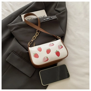 Detail der Erdbeerdruck-Schultertasche mit goldener Kette auf grauem Blazer