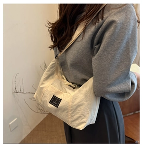Detail of a cream canvas crossbody tote bag showing fabric texture and adjustable strap
