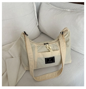 Close-up of beige nylon hobo bag featuring a black logo patch and front pocket detail