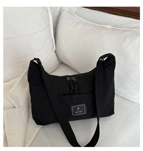 Close-up of black nylon tote bag with brand label on a minimalist bed background