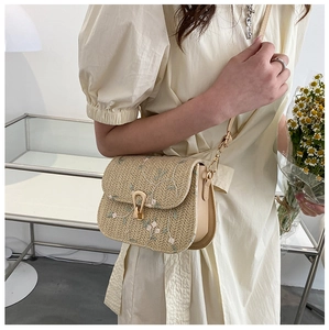 Detail of straw saddle bag featuring floral embroidery and elegant metal clasp