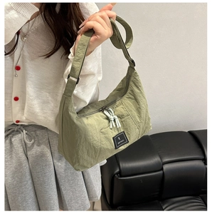 Detail of olive green nylon crossbody bag featuring woven logo patch and knot zipper pulls