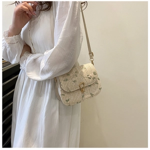 Detail of straw woven saddle bag with green floral embroidery and metal buckle
