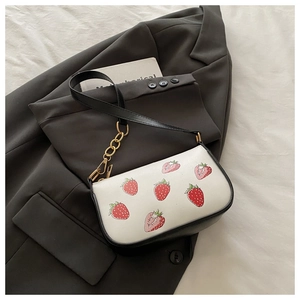 Detail der weißen Handtasche mit Erdbeerdruck, schwarzem Gurt und goldener Kette am Blazer