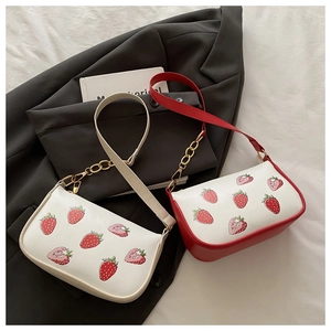 Detail der cremefarbenen Erdbeerdruck-Handtasche mit goldener Metallkette auf einem Blazer