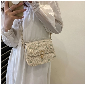 Detail of summer straw saddle bag with floral embroidery and gold heart clasp on a model