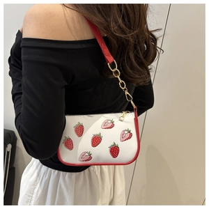 Model trägt eine weiß-rote Schultertasche mit Erdbeerdruck und goldener Kettenträger