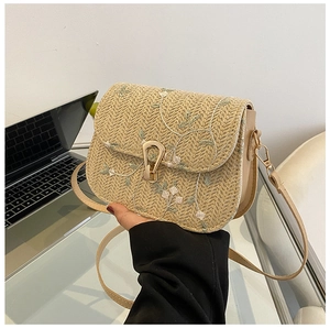 Detail of straw saddle bag with delicate floral embroidery and gold horseshoe buckle