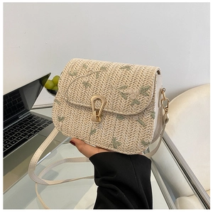 Detailed view of handmade straw saddle bag with green floral embroidery and metal lock
