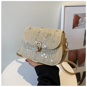 Macro detail of straw woven saddle bag with floral embroidery and golden metal lock