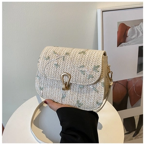 Close-up of beige woven saddle bag featuring delicate green floral embroidery and gold U-buckle