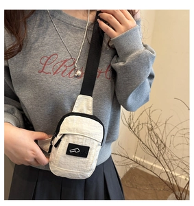 Sac de poitrine minimaliste en nylon beige avec bandoulière noire porté par un mannequin