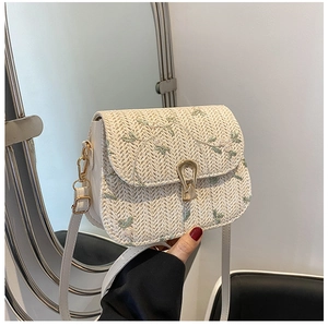 Close-up of beige woven crossbody bag featuring green floral embroidery and gold buckle