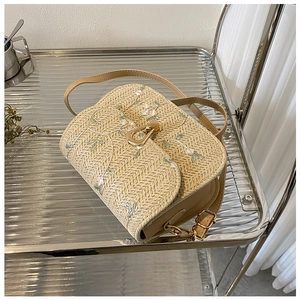 Detail of beige straw saddle bag featuring floral embroidery and golden metal clasp buckle
