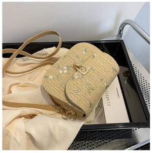 Detail of straw saddle bag with white floral embroidery and gold metal U-shaped clasp
