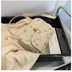 Detailed straw weave pattern and green floral embroidery on an elegant beige saddle bag