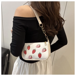 Side view of a white shoulder bag with strawberry print and gold chain strap on model