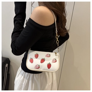 Detail view of strawberry print white shoulder bag with gold chain strap on a model