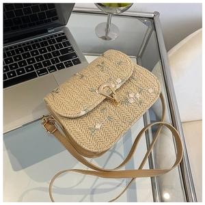 Close-up of beige straw saddle bag with delicate floral embroidery and gold metal lock