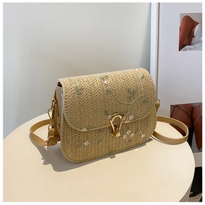 Detail of beige straw saddle bag featuring white floral embroidery and gold metal clasp