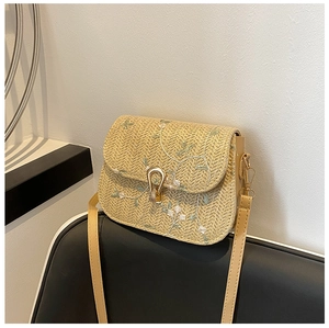 Detail of straw crossbody bag featuring green floral embroidery and gold metal clasp