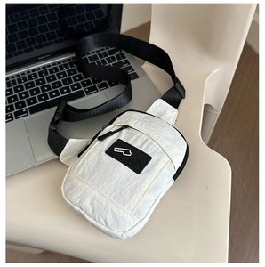 Vue détaillée d'un sac de poitrine en nylon blanc avec sangle noire sur une chaise