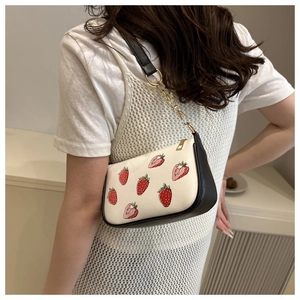 Close-up of strawberry print handbag with gold chain strap worn by a model