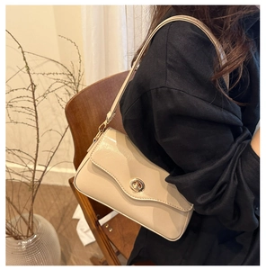 Détail d'un sac porté épaule crème avec fermoir rotatif doré sur cuir lisse brillant