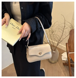 Détail d'un sac à bandoulière crème avec fermoir doré porté par un mannequin en noir
