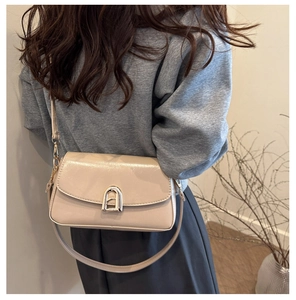 Détail d'un sac bandoulière en cuir verni crème avec un fermoir en arche argenté sur modèle