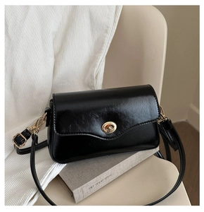 Détail du sac baguette noir brillant avec texture huilée et fermoir en métal doré
