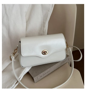 Détail du cuir grainé blanc et du fermoir rotatif en métal doré sur le sac bandoulière
