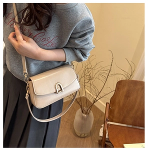 Sac bandoulière beige en similicuir avec fermoir doré porté par un mannequin chic