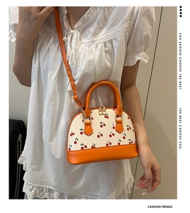 Detail of mini cherry print crossbody bag with orange handles and adjustable strap