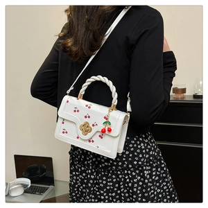 Detailed view of white cherry print crossbody bag with twist handle and metal clasp